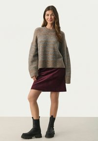 Bruin en blauw gestreepte gebreide trui met geribbelde zoom, gecombineerd met een bordeauxkleurige corduroy rok en zwarte stevige enkellaarsjes.