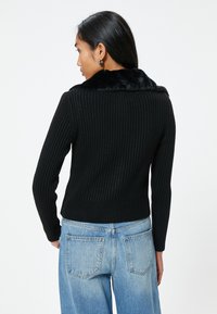 Maglione nero a coste con collo in pelliccia sintetica, design aderente, maniche lunghe e lunghezza crop, abbinato a jeans blu a vita alta.