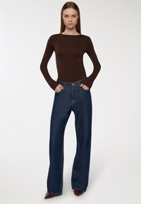 Maglietta marrone a maniche lunghe abbinata a jeans a vita alta blu scuro con gamba larga. I jeans sono dotati di chiusura con bottone e tasche frontali.