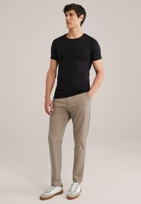 T-shirt noir à manches courtes associé à un pantalon beige clair et des baskets grises/blanches, avec une coupe slim et une texture de tissu lisse.