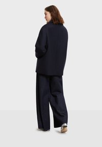 Námornícky vlnený oversize kabát s vysokým golierom, skombinovaný so širokými tmavými džínsami a topánkami s metalickými akcentmi. Jednoduchý dizajn.