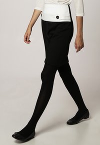 Svarta skräddarsydda shorts med vit midja, prydda med två runda svarta knappar. Slät tyg, i kombination med svarta strumpbyxor och lägenheter.