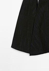 Zwart gestreepte stof met zilveren draaddetails, met een vloeiende, asymmetrische snit en een gladde textuur voor een gestructureerd uiterlijk.