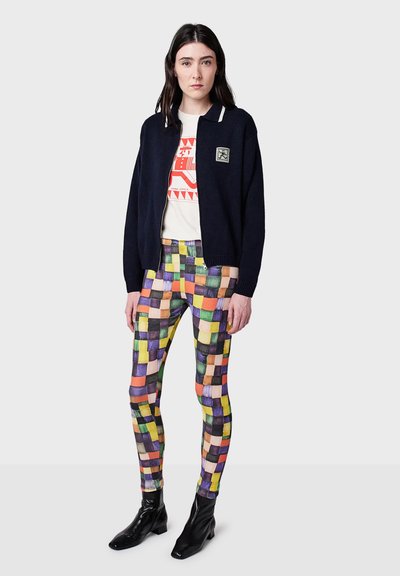 Marinblå cardigan med vit krage, mönstrade leggings i livliga färger och svarta ankelskor. Detaljerad grafik på vit t-shirt under.