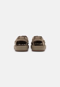 Brown sandals with a textured upper, adjustable straps, and cut-out details, featuring a cushioned sole and rubber traction outsole.