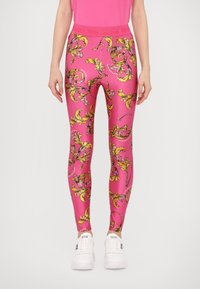 Leggings rosa realizzati in tessuto elasticizzato, con un elaborato motivo floreale giallo e nero, una vita alta e sneaker bianche da attivit sportiva.