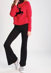Felpa rossa con grafica di renne nere e stelle. Pantaloni neri a campana e sneakers argento completano l'outfit.