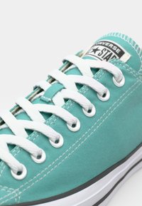 Teal canvas sneaker with white laces, metal eyelets, and a black label displaying the Converse star logo. Features white stitching and a rubber sole.