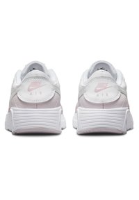 Baskets Nike blanches avec des accents roses, dotées d'une tige en cuir lisse, d'un col rembourré et d'une semelle en caoutchouc texturée avec des rayures.