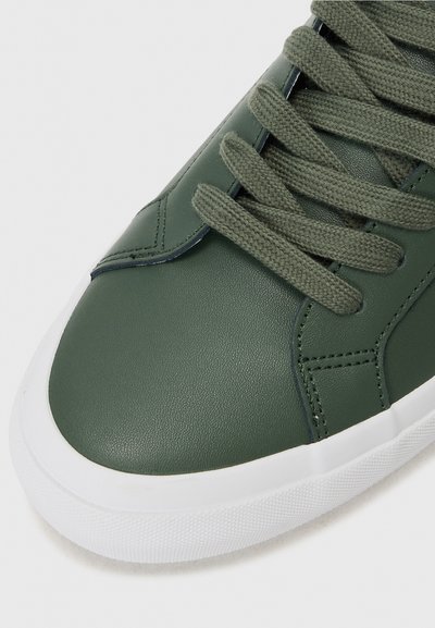 Green faux leather sneaker with flat olive laces, textured upper, white rubber sole, and subtle stitching detail along the sides.