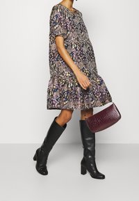 Schwarze knielange Stiefel, kurzärmliges Kleid mit floralem Muster in dunklen Tönen, geraffter Saum, glatte Textur und eine strukturierte Handtasche in Burgunderrot.