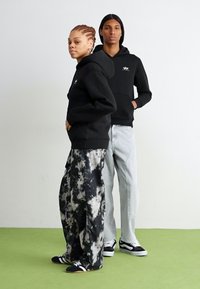 Sweatshirts à capuche noirs, pantalons tie-dye avec des motifs noir et blanc, jeans clairs et baskets noires. Style simple, décontracté et à coupe ample.