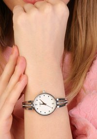 Silver watch with a round white dial, black hands, and dot markers. Features a dual strap with embedded crystals and a polished finish.