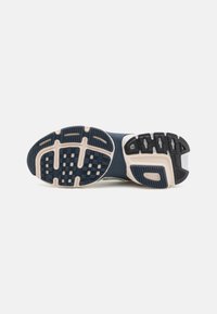 Semelle d'une chaussure de sport bleu marine et beige montrant une bande de roulement en caoutchouc texturée conçue pour la traction et le soutien.