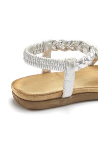 Silberne metallic flache Sandale mit geflochtenen Riemen, gepolstertem Wildlederfußbett und Gummisohle. Merkmale sind ein minimalistisches Design und einfache Akzente.