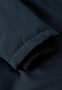Marinblå jackärm med en slät yttre yta och mjukt svart innerfoder. Ärmens kant har en sydd kant med elastiska detaljer för en tät passform.
