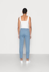 Blauwe broek met een aansluitende taille en taps toelopende pijpen, gemaakt van een gladde stof. Gepaard met een witte tanktop. Geen zichtbare patronen of hardware.