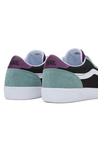 Sneaker in suede neri e teal con accenti bianchi, caratterizzate da un tallone viola e un logo, progettate con una silhouette a bassa punta e colletto imbottito.