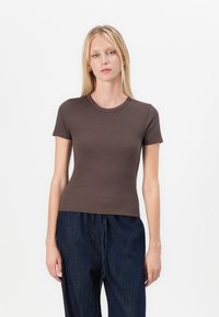 Brun ribbad kortärmad t-shirt med rund halsringning, figurnära design och slät textur, tillsammans med lösa mörka denimbyxor.