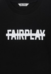 Čierne bavlnené tričko s výrazným bielym textom "FAIRPLAY" navrhnutým s prekrývajúcimi sa písmenami. Kolo výstrih s viditeľnou štítkom.