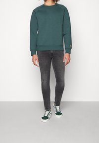 Groene katoenen sweatshirt met ribbels aan de manchetten, gecombineerd met slim-fit grijze jeans en groene suède sneakers met witte zolen en veters.