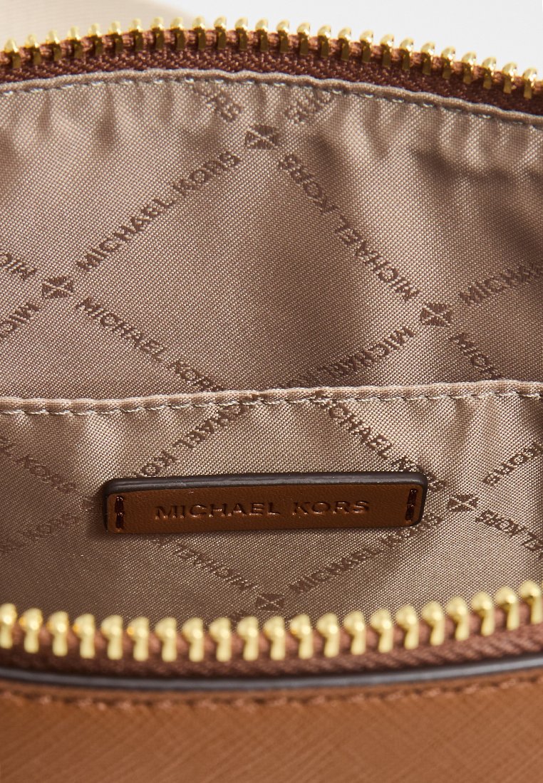 Intérieur en tissu marron avec une fermeture éclair dorée. Présente une étiquette texturée beige avec "MICHAEL KORS" en relief. Motif logo subtil dans la doublure.