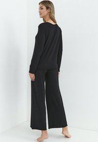 Czarny komplet do relaksu składający się z bluzki z długim rękawem i spodni o szerokich nogawkach, wykonany z miękkiego materiału o gładkiej fakturze. Prosty design bez wzorów.
