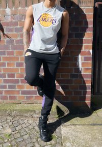 Szary bezrękawnik z logo "Los Angeles Lakers", w połączeniu z czarnymi dresami z purpurowymi paskami po bokach. Czarne wysokie sneakersy.