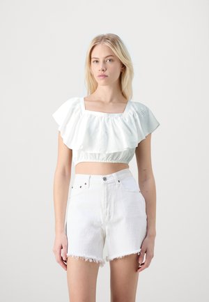 Top alb scurt cu mâneci volan și decolteu pătrat; asortat cu pantaloni scurți din denim albi, cu talie înaltă, cu margine tăiată.