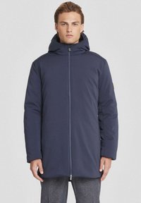 Cappotto imbottito blu navy con colletto alto e cappuccio, dotato di zip centrale e tasche laterali. Texture liscia con silhouette affusolata.