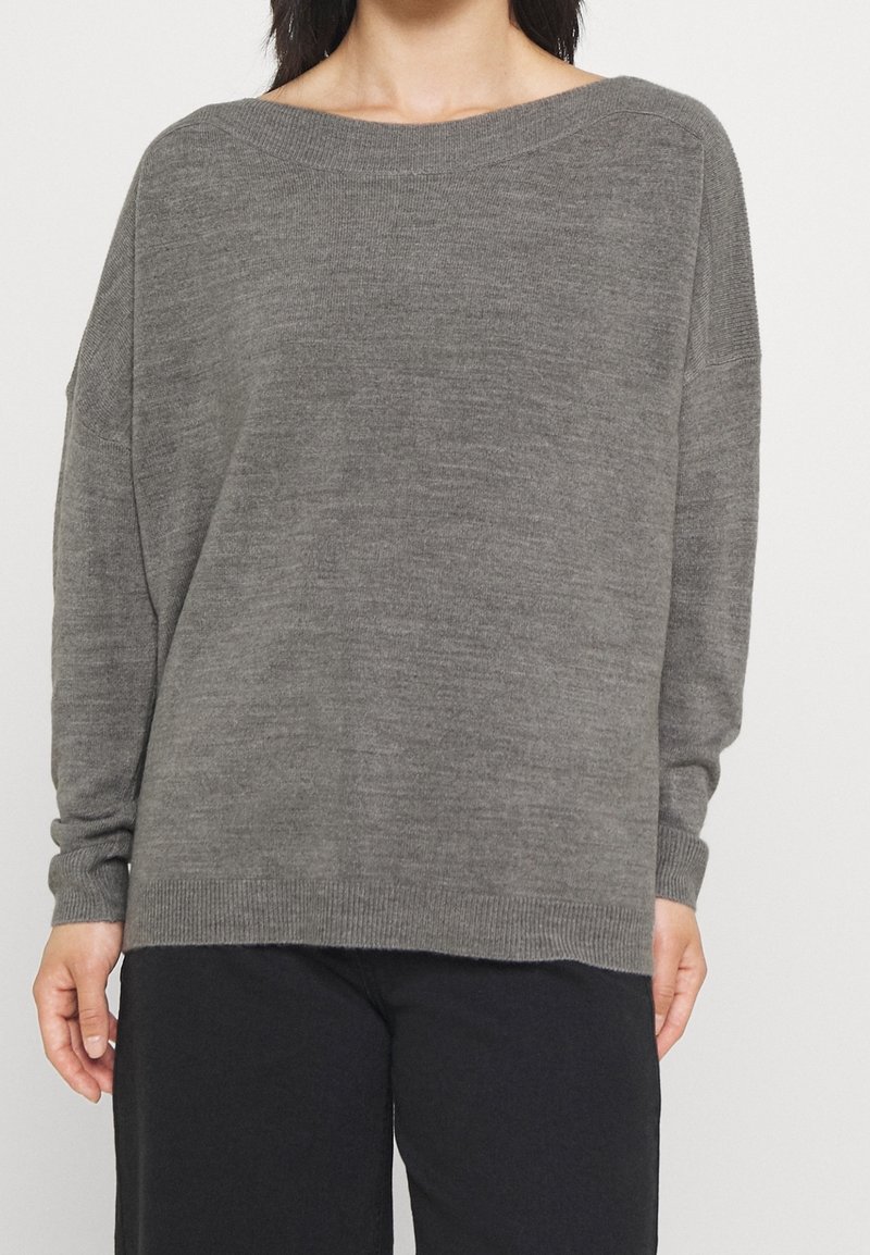 Grau gestrickter Pullover mit weitem Bootsausschnitt, langen Ärmeln und gerippten Bündchen. Weiche Textur und lässige Passform, kombiniert mit schwarzen Hosen.