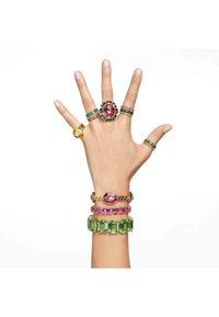 Collection of colorful rings and bracelets: gold, green, pink, and yellow stones with various designs on a hand against a white background.