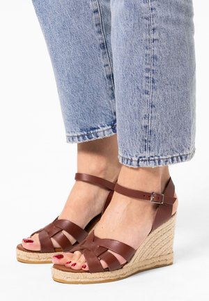 Brown leather wedge sandals with a woven jute platform and ankle strap, featuring a crisscross design on the toe area.