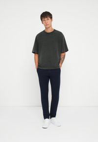 T-shirt nera oversize, tessuto morbido, collo rotondo. Abbinata a pantaloni slim-fit blu navy, tessuto liscio, e sneakers bianche. Design semplice.