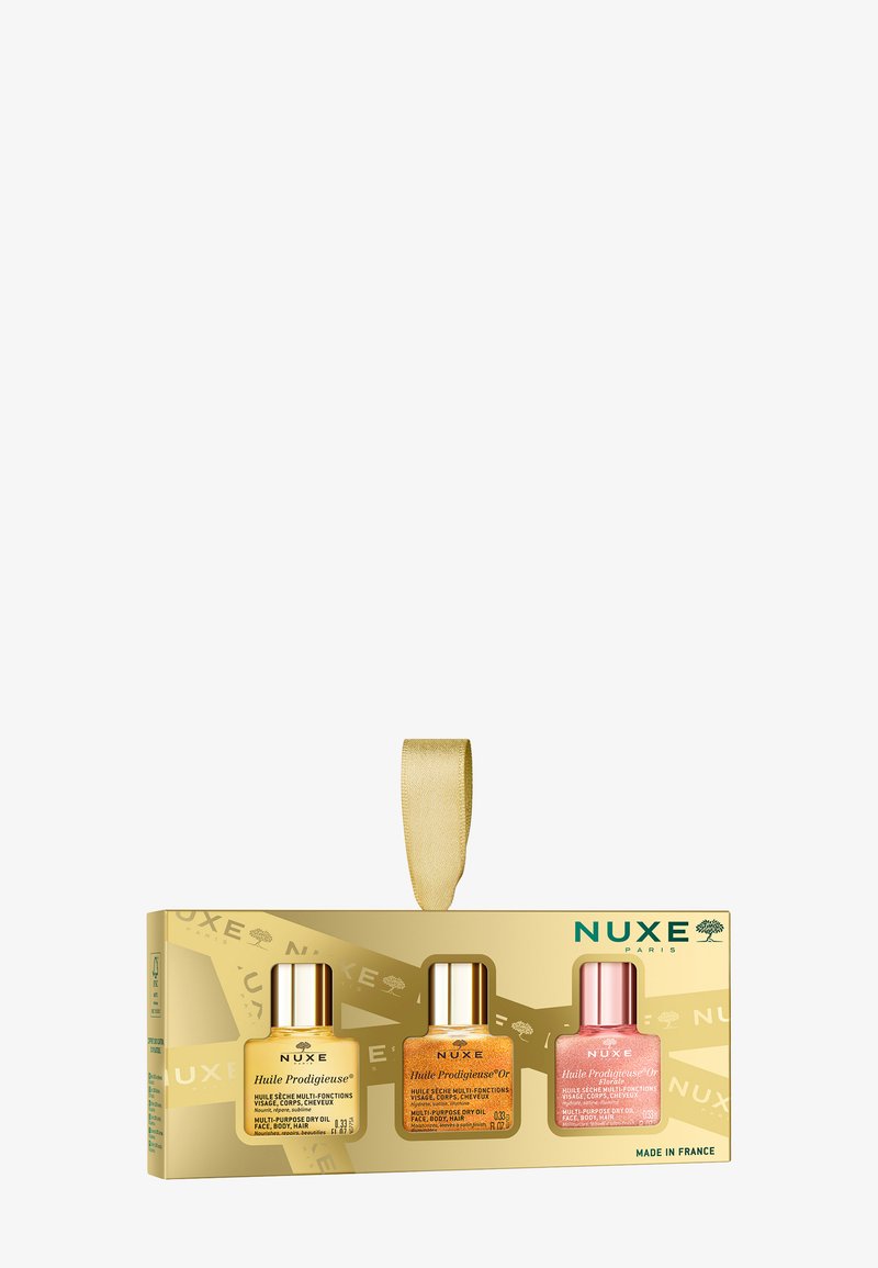 Zestaw trzech szklanych butelek olejków NUXE w złotej pudełku wzorzystym z satynową wstążką. Butelki są w kolorze żółtym, złotym i różowym.