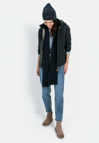 Donkere gewatteerde jas, marineblauwe gebreide beanie, gestreepte top, lange donkere sjaal, lichte jeans en brown enkellaarsjes. Eenvoudige, functionele winteroutfit.