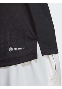 Černé atletické tričko s technologií odvádění vlhkosti Aeroready. Má puntíkovanou texturu, přišitý lem a bílé logo vlevo dole.