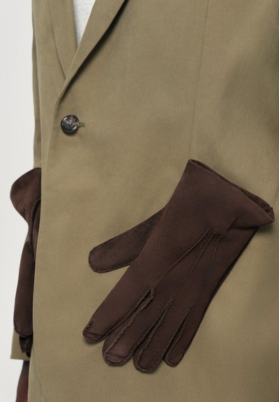 Braune Wildledersitze, die auf einer hellolivgrünen Jacke präsentiert werden, die über einen Knopfverschluss und elegante Designelemente verfügt.