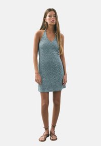 Robe halter bleu clair avec une silhouette ajustée, tissu texturé présentant un motif de petites paillettes, et un décolleté en V.