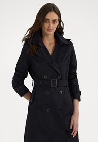 Marine trenchcoat gemaakt van duurzaam materiaal, met dubbelgeknoopte knopen, een ceintuur in de taille en een brede kraag met schouderepauletten.