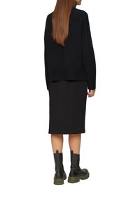 Schwarzer gestrickter Oversize-Pullover kombiniert mit einem schwarzen strukturierten Bleistiftrock, ergänzt durch schwarze und olivgrüne klobige Stiefeletten.