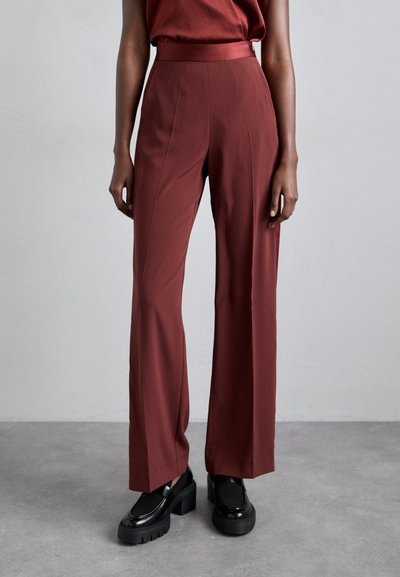 Pantalons larges bordeaux avec une texture lisse et une taille haute, associés à des mocassins noirs épais sur un sol gris.