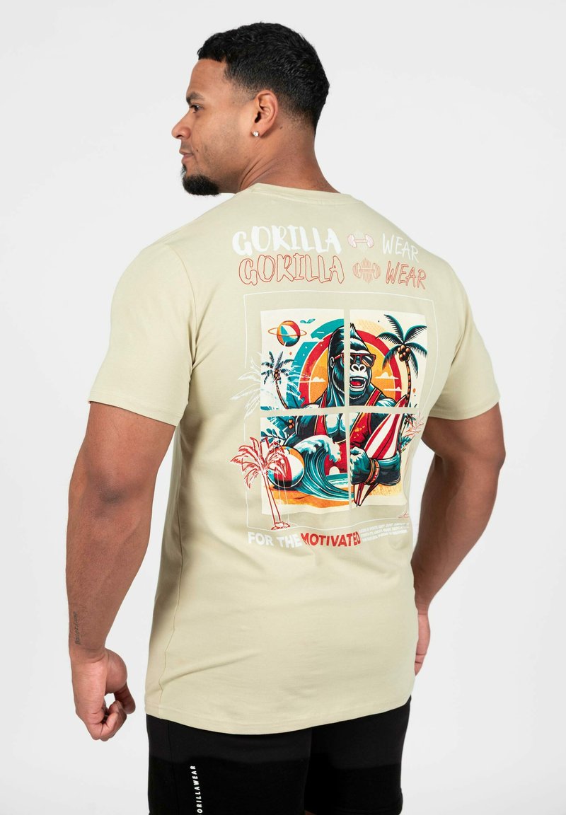 Licht beige katoenen T-shirt met een kleurrijke gorilla graphic, palmbomen, golven en een surfplank, met de tekst "VOOR DE GEMOTIVEERDEN."