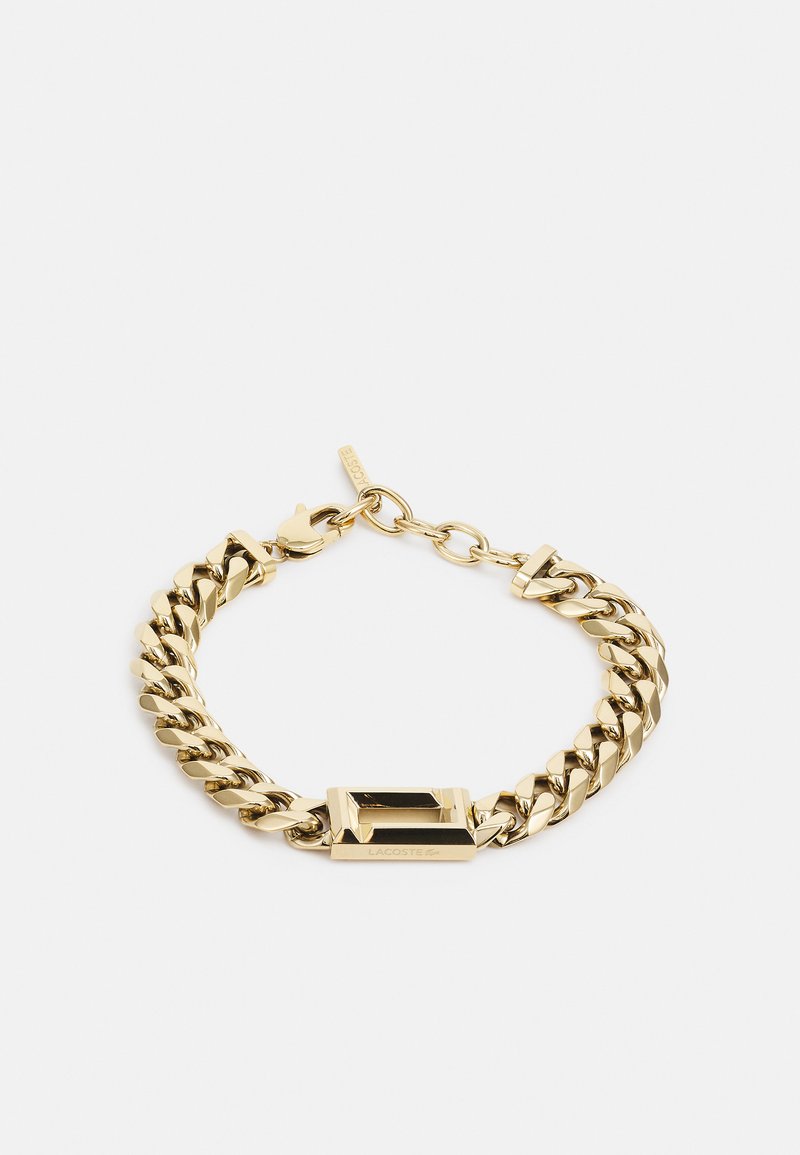 Pulsera de cadena en tono dorado con un cierre rectangular plano y eslabones pulidos. El diseño tiene una textura suave y un estilo entrelazado.