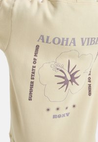 Felpa beige con colletto a coste. Presenta grafiche floreali viola e testi che includono "ALOHA VIBES" e "STATE OF MIND ESTIVA."