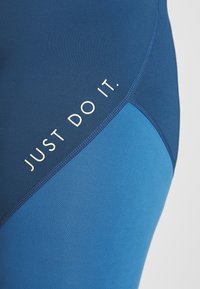Granatowe i jasnoniebieskie legginsy wykonane z rozciągliwego materiału, z wyraźnym białym napisem "JUST DO IT." wzdłuż szwu oraz płaskimi szwami.