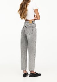 Jeans de tiro alto de color gris claro con pierna recta, diseño de cinco bolsillos y una etiqueta de cuero color marrón en la cinturilla trasera. Se llevan zapatos negros.