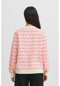 Pull en maille crème avec un motif de nœud rose répété, design oversized, col et poignets côtelés, et longues manches bouffantes.