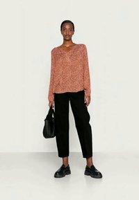 Blusa de manga longa, com decote em V na cor ferrugem com padrão floral branco; combinada com calças tapered pretas e sapatos plataforma pretos. Mala preta.