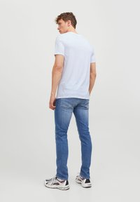 T-shirt bleu clair à manches courtes en tissu doux, associé à un jean slim délavé et à des chaussures de sport multicolores.